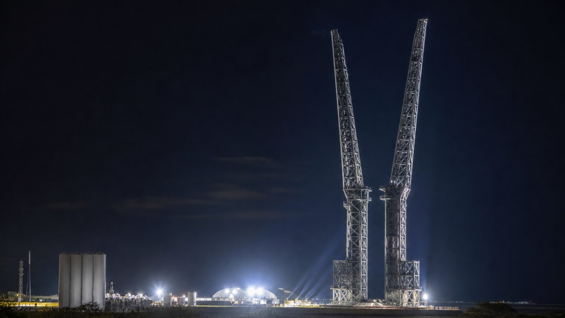 Two floodlit catch towers at night with arms raised