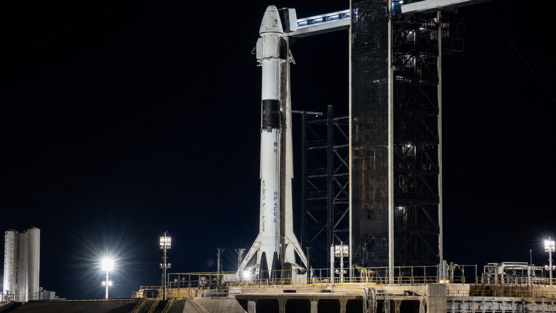 A Falcon 9 and Crew Dragon vertical on a floodlit pad